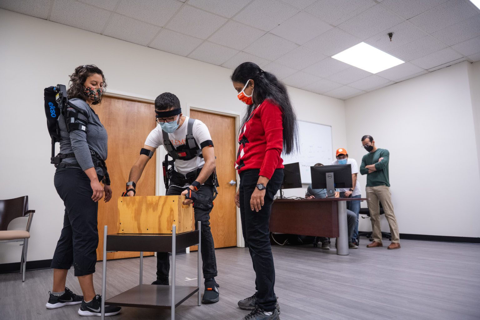 Jessica Avilés (left) and Divya Srinivasan (right) demonstrate their exoskeleton research with a student’s help. (Photo from Clemson University)