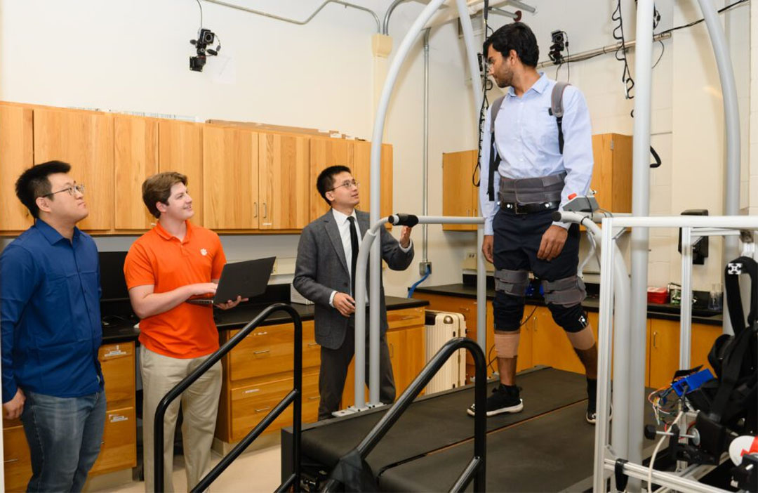 Hamdan Khan wears an exoskeleton while walking on a treadmill in Ge Lv’s lab while Ph.D. student Miao Yu (far left) and undergraduate Tapp Rhoads (second from left) and Lv watch and discuss their research (Photo from Clemson University)