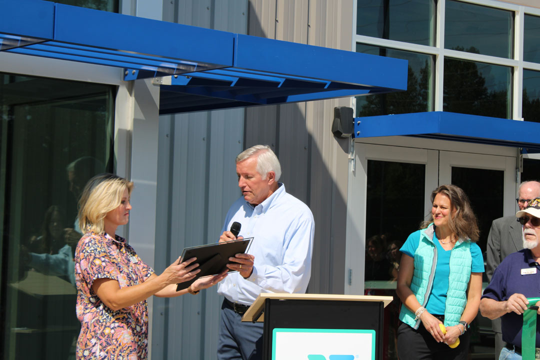 Rick Cothran, Director of Membership and Engagement with the Easley Chamber of Commerce, presents Kim Valentin with a gift of $1 from the Easley Chamber of Commerce. (Photo by Karen Brewer, The Pickens County Chronicle)