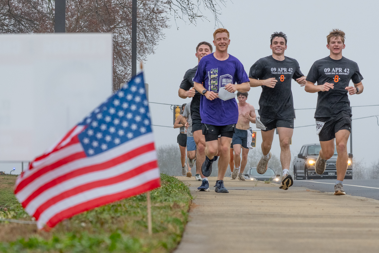 Hundreds of people participate in the 2026 Clemson 8 Challenge, an eight-mile run/walk/ruck march, on a misty Saturday morning, March 7, 2026. The Challenge was created to honor the 25 known Clemson alumni who suffered as POWs in all wars. It was originally created for 1938 Clemson alumnus, professor emeritus and WWII hero Ben Skardon, a survivor of the Bataan Death March, but has expanded to include Clemson POWs from all wars. Money raised from the event goes toward sending teams of Clemson ROTC students to participate in the Bataan Memorial Death March at White Sands Missile Range, NM. Sophomore finance major GB Stalnaker served as master of ceremonies. (Photo by Ken Scar)