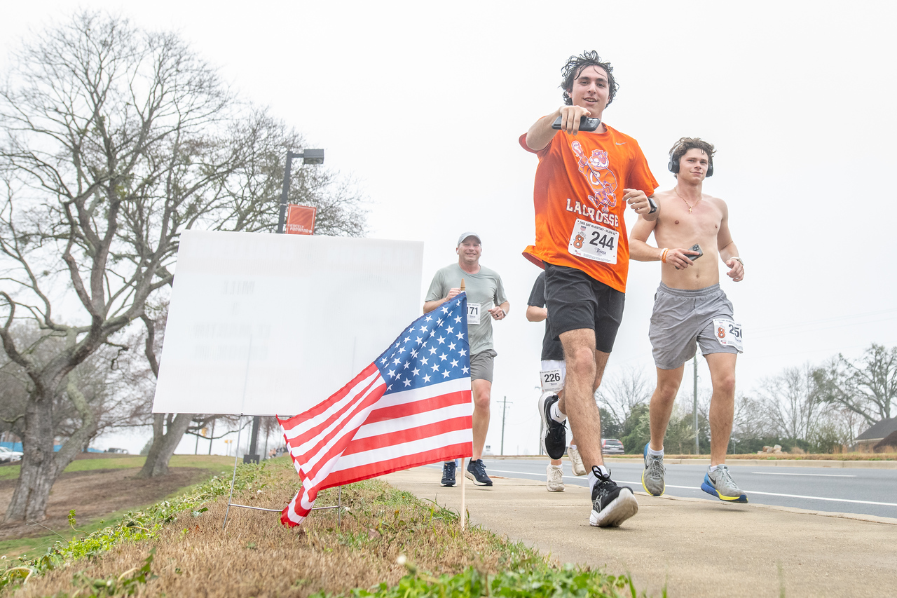 Hundreds of people participate in the 2026 Clemson 8 Challenge, an eight-mile run/walk/ruck march, on a misty Saturday morning, March 7, 2026. The Challenge was created to honor the 25 known Clemson alumni who suffered as POWs in all wars. It was originally created for 1938 Clemson alumnus, professor emeritus and WWII hero Ben Skardon, a survivor of the Bataan Death March, but has expanded to include Clemson POWs from all wars. Money raised from the event goes toward sending teams of Clemson ROTC students to participate in the Bataan Memorial Death March at White Sands Missile Range, NM. Sophomore finance major GB Stalnaker served as master of ceremonies. (Photo by Ken Scar)