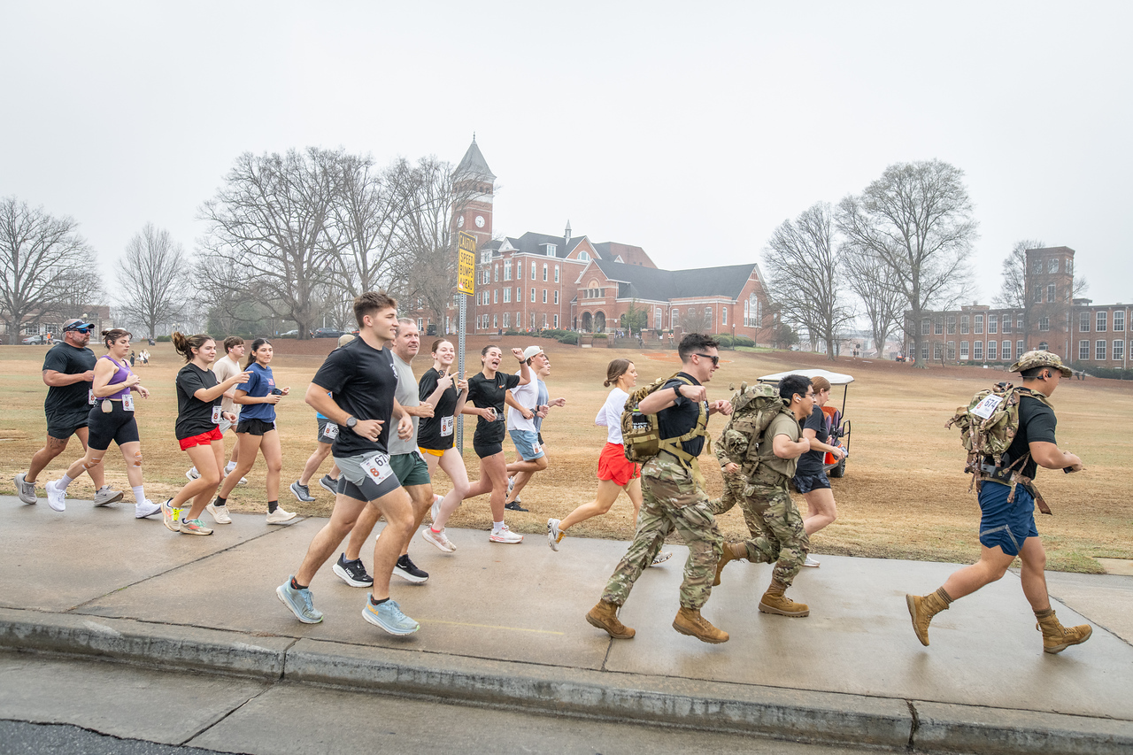 Hundreds of people participate in the 2026 Clemson 8 Challenge, an eight-mile run/walk/ruck march, on a misty Saturday morning, March 7, 2026. The Challenge was created to honor the 25 known Clemson alumni who suffered as POWs in all wars. It was originally created for 1938 Clemson alumnus, professor emeritus and WWII hero Ben Skardon, a survivor of the Bataan Death March, but has expanded to include Clemson POWs from all wars. Money raised from the event goes toward sending teams of Clemson ROTC students to participate in the Bataan Memorial Death March at White Sands Missile Range, NM. Sophomore finance major GB Stalnaker served as master of ceremonies. (Photo by Ken Scar)