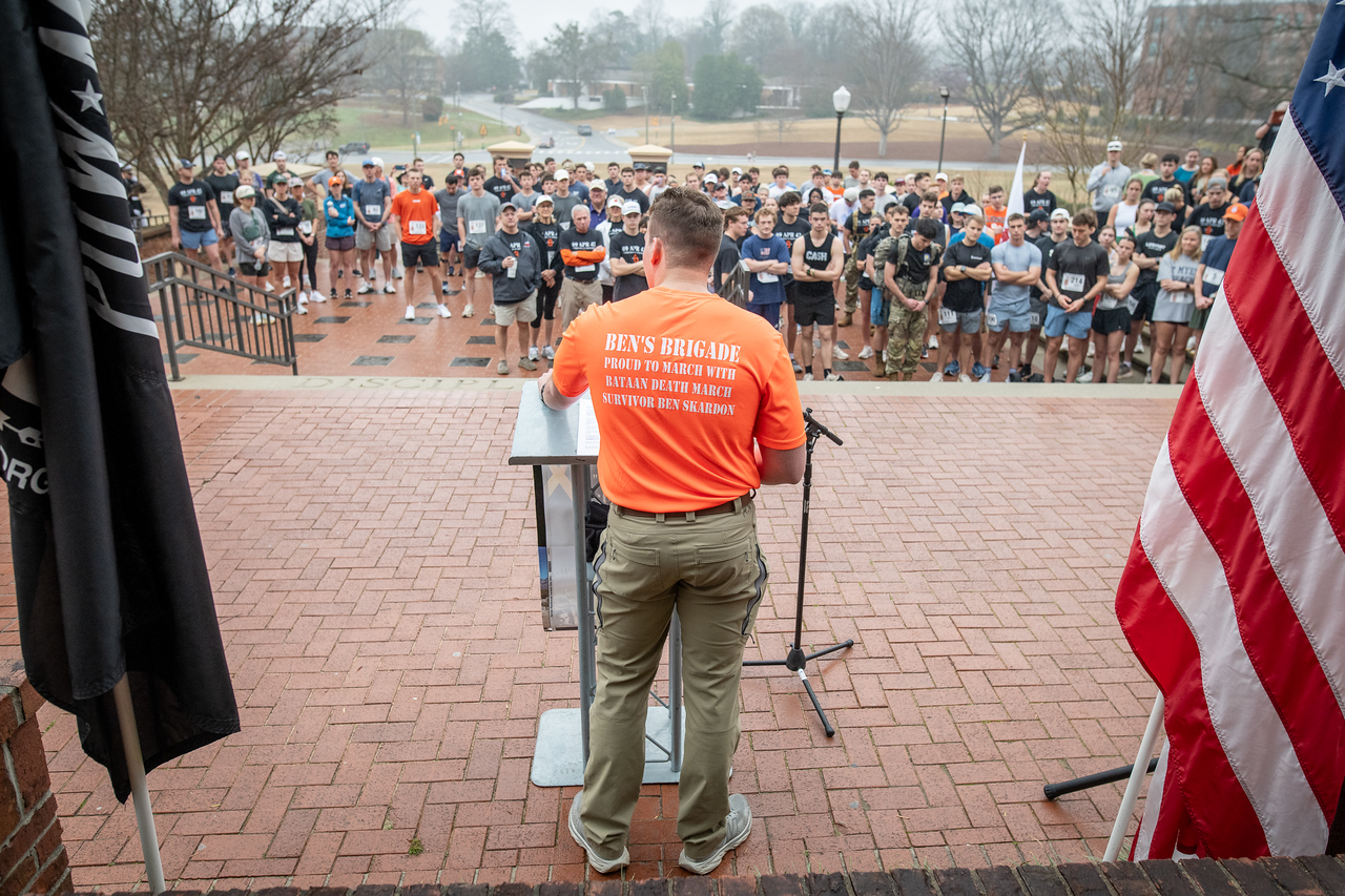 Hundreds of people participate in the 2026 Clemson 8 Challenge, an eight-mile run/walk/ruck march, on a misty Saturday morning, March 7, 2026. The Challenge was created to honor the 25 known Clemson alumni who suffered as POWs in all wars. It was originally created for 1938 Clemson alumnus, professor emeritus and WWII hero Ben Skardon, a survivor of the Bataan Death March, but has expanded to include Clemson POWs from all wars. Money raised from the event goes toward sending teams of Clemson ROTC students to participate in the Bataan Memorial Death March at White Sands Missile Range, NM. Sophomore finance major GB Stalnaker served as master of ceremonies. (Photo by Ken Scar)
