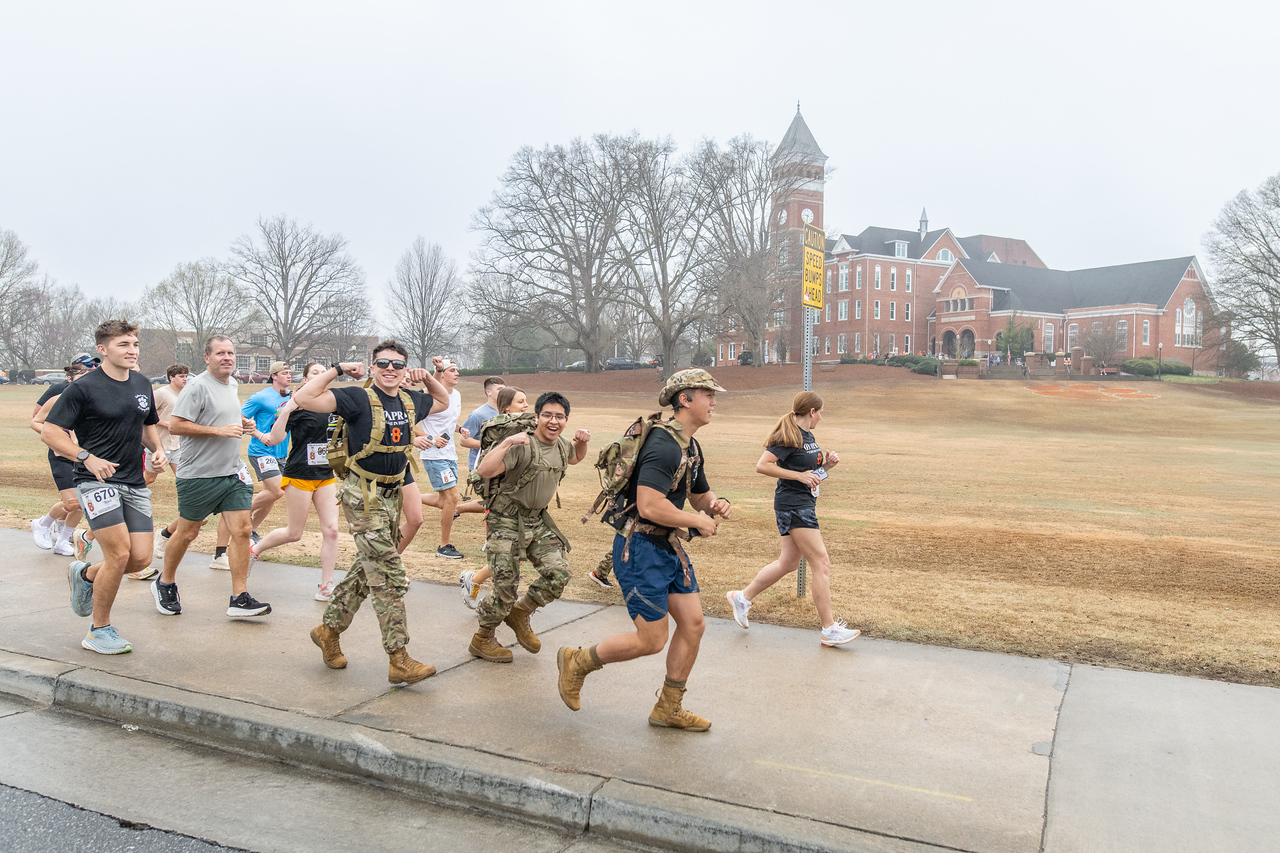 Hundreds of people participate in the 2026 Clemson 8 Challenge, an eight-mile run/walk/ruck march, on a misty Saturday morning, March 7, 2026. The Challenge was created to honor the 25 known Clemson alumni who suffered as POWs in all wars. It was originally created for 1938 Clemson alumnus, professor emeritus and WWII hero Ben Skardon, a survivor of the Bataan Death March, but has expanded to include Clemson POWs from all wars. Money raised from the event goes toward sending teams of Clemson ROTC students to participate in the Bataan Memorial Death March at White Sands Missile Range, NM. Sophomore finance major GB Stalnaker served as master of ceremonies. (Photo by Ken Scar)