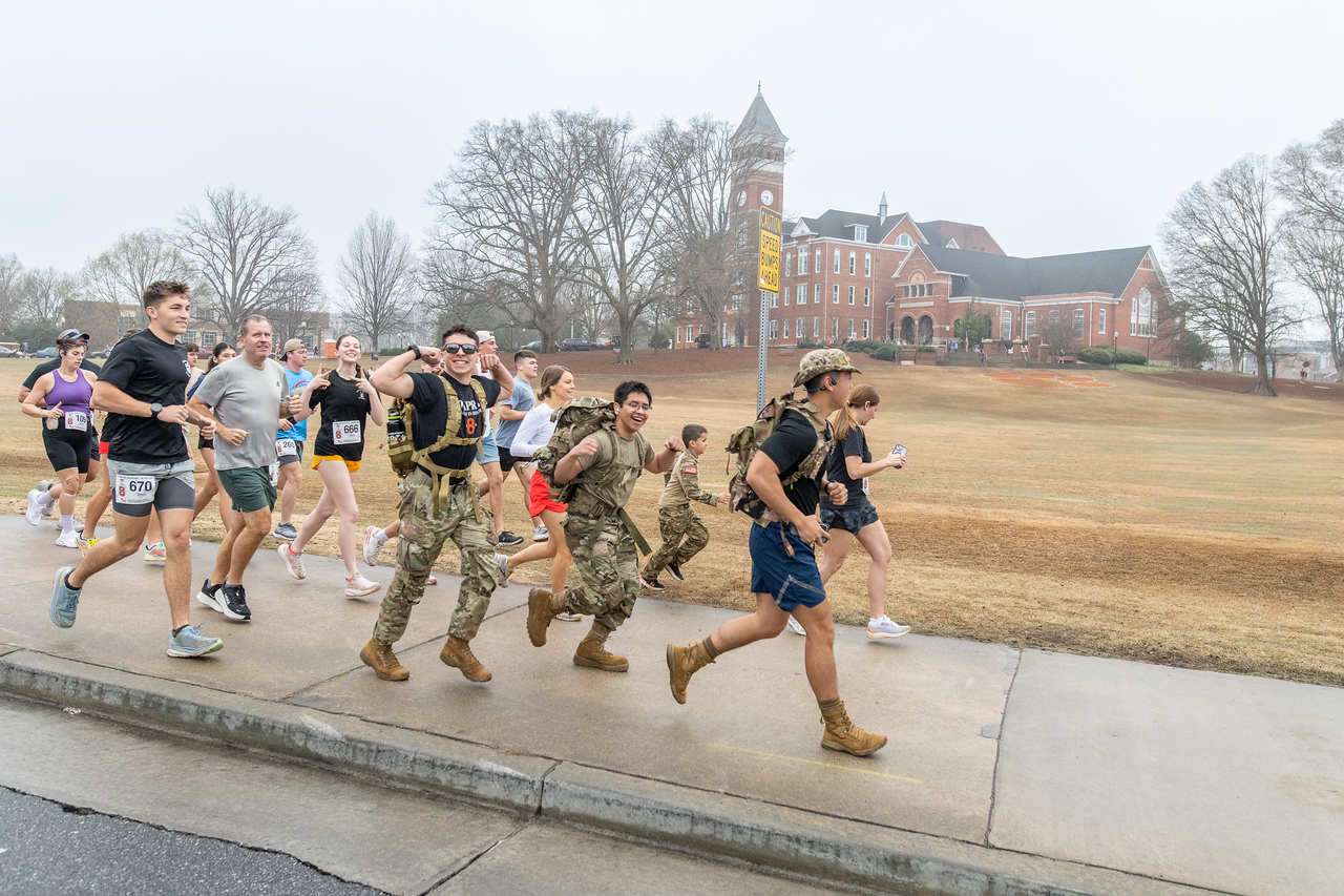 Hundreds of people participate in the 2026 Clemson 8 Challenge, an eight-mile run/walk/ruck march, on a misty Saturday morning, March 7, 2026. The Challenge was created to honor the 25 known Clemson alumni who suffered as POWs in all wars. It was originally created for 1938 Clemson alumnus, professor emeritus and WWII hero Ben Skardon, a survivor of the Bataan Death March, but has expanded to include Clemson POWs from all wars. Money raised from the event goes toward sending teams of Clemson ROTC students to participate in the Bataan Memorial Death March at White Sands Missile Range, NM. Sophomore finance major GB Stalnaker served as master of ceremonies. (Photo by Ken Scar)