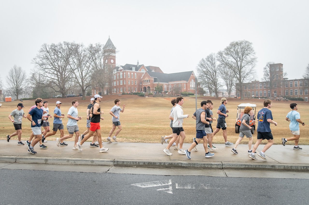 Hundreds of people participate in the 2026 Clemson 8 Challenge, an eight-mile run/walk/ruck march, on a misty Saturday morning, March 7, 2026. The Challenge was created to honor the 25 known Clemson alumni who suffered as POWs in all wars. It was originally created for 1938 Clemson alumnus, professor emeritus and WWII hero Ben Skardon, a survivor of the Bataan Death March, but has expanded to include Clemson POWs from all wars. Money raised from the event goes toward sending teams of Clemson ROTC students to participate in the Bataan Memorial Death March at White Sands Missile Range, NM. Sophomore finance major GB Stalnaker served as master of ceremonies. (Photo by Ken Scar)