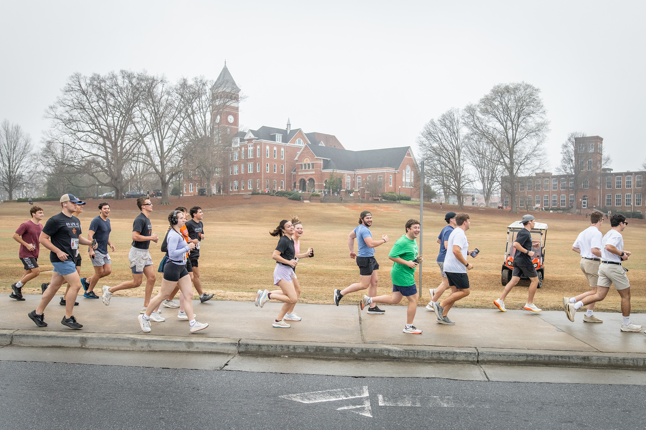 Hundreds of people participate in the 2026 Clemson 8 Challenge, an eight-mile run/walk/ruck march, on a misty Saturday morning, March 7, 2026. The Challenge was created to honor the 25 known Clemson alumni who suffered as POWs in all wars. It was originally created for 1938 Clemson alumnus, professor emeritus and WWII hero Ben Skardon, a survivor of the Bataan Death March, but has expanded to include Clemson POWs from all wars. Money raised from the event goes toward sending teams of Clemson ROTC students to participate in the Bataan Memorial Death March at White Sands Missile Range, NM. Sophomore finance major GB Stalnaker served as master of ceremonies. (Photo by Ken Scar)