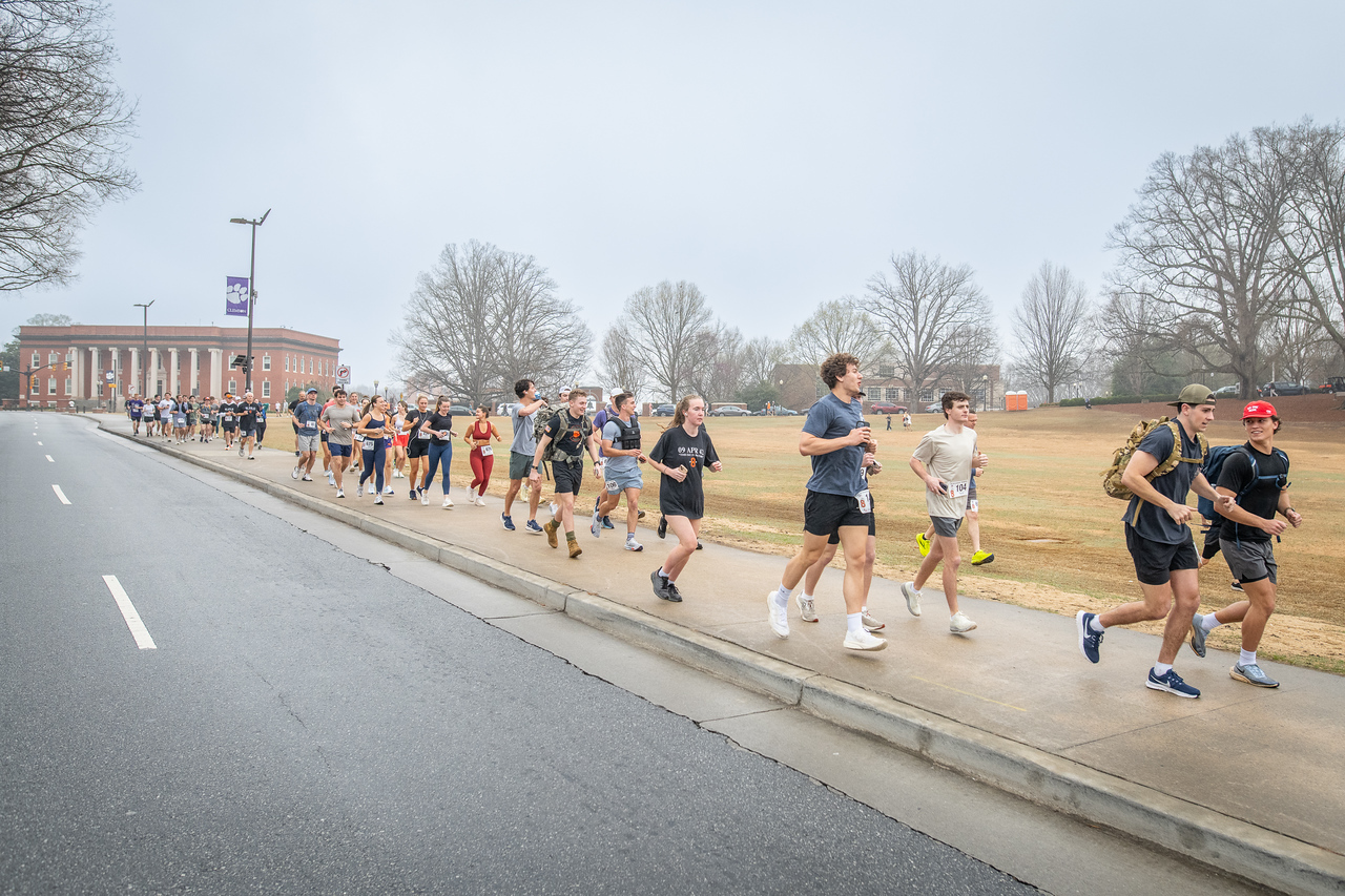 Hundreds of people participate in the 2026 Clemson 8 Challenge, an eight-mile run/walk/ruck march, on a misty Saturday morning, March 7, 2026. The Challenge was created to honor the 25 known Clemson alumni who suffered as POWs in all wars. It was originally created for 1938 Clemson alumnus, professor emeritus and WWII hero Ben Skardon, a survivor of the Bataan Death March, but has expanded to include Clemson POWs from all wars. Money raised from the event goes toward sending teams of Clemson ROTC students to participate in the Bataan Memorial Death March at White Sands Missile Range, NM. Sophomore finance major GB Stalnaker served as master of ceremonies. (Photo by Ken Scar)