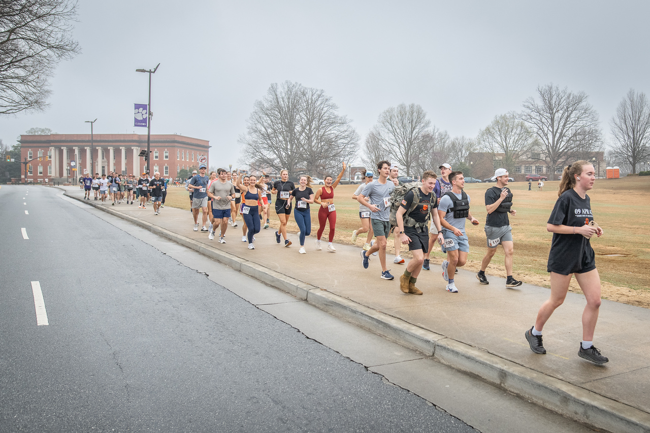 Hundreds of people participate in the 2026 Clemson 8 Challenge, an eight-mile run/walk/ruck march, on a misty Saturday morning, March 7, 2026. The Challenge was created to honor the 25 known Clemson alumni who suffered as POWs in all wars. It was originally created for 1938 Clemson alumnus, professor emeritus and WWII hero Ben Skardon, a survivor of the Bataan Death March, but has expanded to include Clemson POWs from all wars. Money raised from the event goes toward sending teams of Clemson ROTC students to participate in the Bataan Memorial Death March at White Sands Missile Range, NM. Sophomore finance major GB Stalnaker served as master of ceremonies. (Photo by Ken Scar)