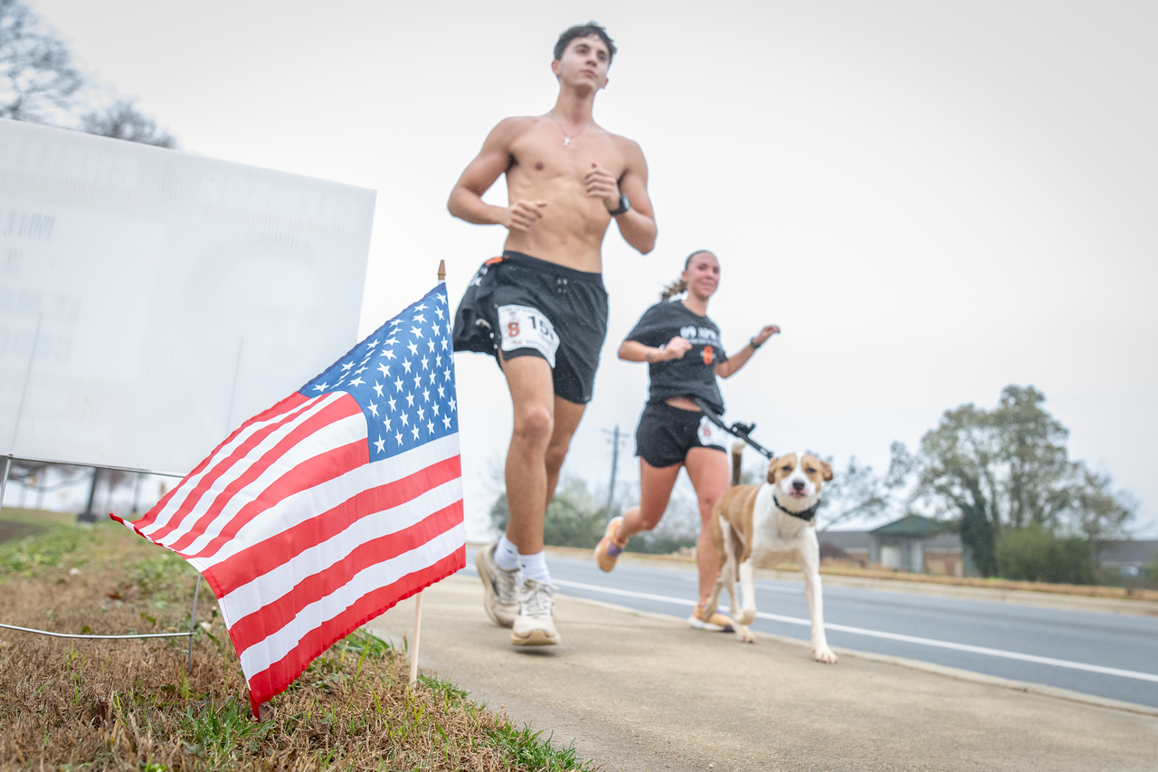Hundreds of people participate in the 2026 Clemson 8 Challenge, an eight-mile run/walk/ruck march, on a misty Saturday morning, March 7, 2026. The Challenge was created to honor the 25 known Clemson alumni who suffered as POWs in all wars. It was originally created for 1938 Clemson alumnus, professor emeritus and WWII hero Ben Skardon, a survivor of the Bataan Death March, but has expanded to include Clemson POWs from all wars. Money raised from the event goes toward sending teams of Clemson ROTC students to participate in the Bataan Memorial Death March at White Sands Missile Range, NM. Sophomore finance major GB Stalnaker served as master of ceremonies. (Photo by Ken Scar)