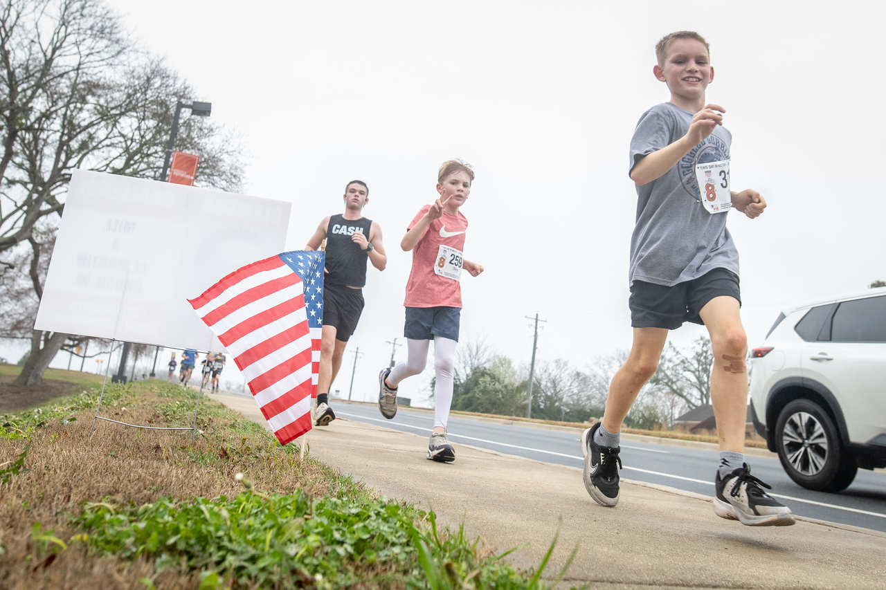 Hundreds of people participate in the 2026 Clemson 8 Challenge, an eight-mile run/walk/ruck march, on a misty Saturday morning, March 7, 2026. The Challenge was created to honor the 25 known Clemson alumni who suffered as POWs in all wars. It was originally created for 1938 Clemson alumnus, professor emeritus and WWII hero Ben Skardon, a survivor of the Bataan Death March, but has expanded to include Clemson POWs from all wars. Money raised from the event goes toward sending teams of Clemson ROTC students to participate in the Bataan Memorial Death March at White Sands Missile Range, NM. Sophomore finance major GB Stalnaker served as master of ceremonies. (Photo by Ken Scar)