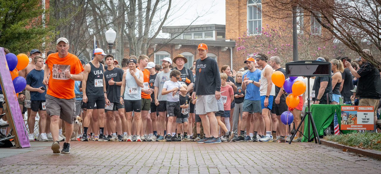Hundreds of people participate in the 2026 Clemson 8 Challenge, an eight-mile run/walk/ruck march, on a misty Saturday morning, March 7, 2026. The Challenge was created to honor the 25 known Clemson alumni who suffered as POWs in all wars. It was originally created for 1938 Clemson alumnus, professor emeritus and WWII hero Ben Skardon, a survivor of the Bataan Death March, but has expanded to include Clemson POWs from all wars. Money raised from the event goes toward sending teams of Clemson ROTC students to participate in the Bataan Memorial Death March at White Sands Missile Range, NM. Sophomore finance major GB Stalnaker served as master of ceremonies. (Photo by Ken Scar)