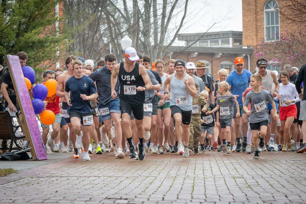 Hundreds of people participate in the 2026 Clemson 8 Challenge, an eight-mile run/walk/ruck march, on a misty Saturday morning, March 7, 2026. The Challenge was created to honor the 25 known Clemson alumni who suffered as POWs in all wars. It was originally created for 1938 Clemson alumnus, professor emeritus and WWII hero Ben Skardon, a survivor of the Bataan Death March, but has expanded to include Clemson POWs from all wars. Money raised from the event goes toward sending teams of Clemson ROTC students to participate in the Bataan Memorial Death March at White Sands Missile Range, NM. Sophomore finance major GB Stalnaker served as master of ceremonies. (Photo by Ken Scar)