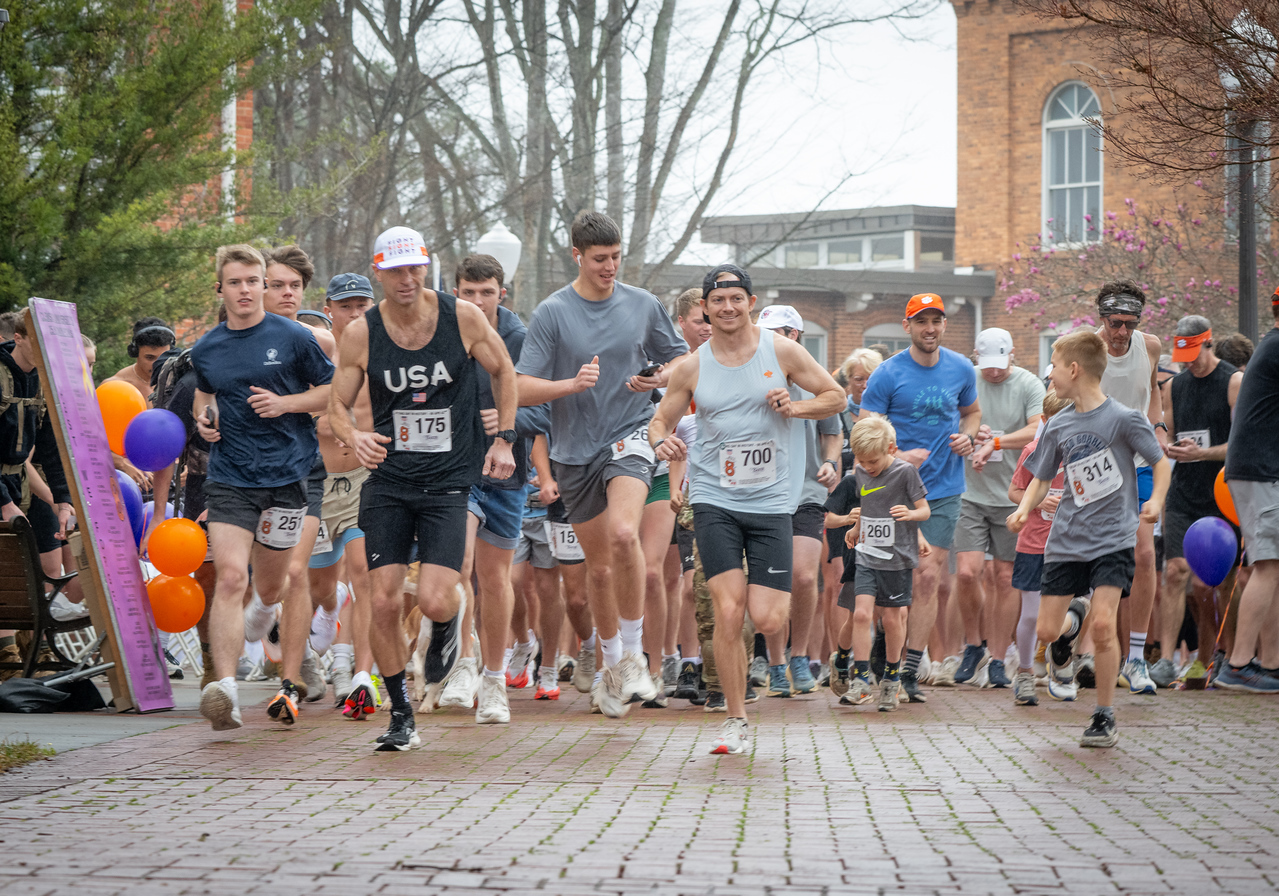 Hundreds of people participate in the 2026 Clemson 8 Challenge, an eight-mile run/walk/ruck march, on a misty Saturday morning, March 7, 2026. The Challenge was created to honor the 25 known Clemson alumni who suffered as POWs in all wars. It was originally created for 1938 Clemson alumnus, professor emeritus and WWII hero Ben Skardon, a survivor of the Bataan Death March, but has expanded to include Clemson POWs from all wars. Money raised from the event goes toward sending teams of Clemson ROTC students to participate in the Bataan Memorial Death March at White Sands Missile Range, NM. Sophomore finance major GB Stalnaker served as master of ceremonies. (Photo by Ken Scar)