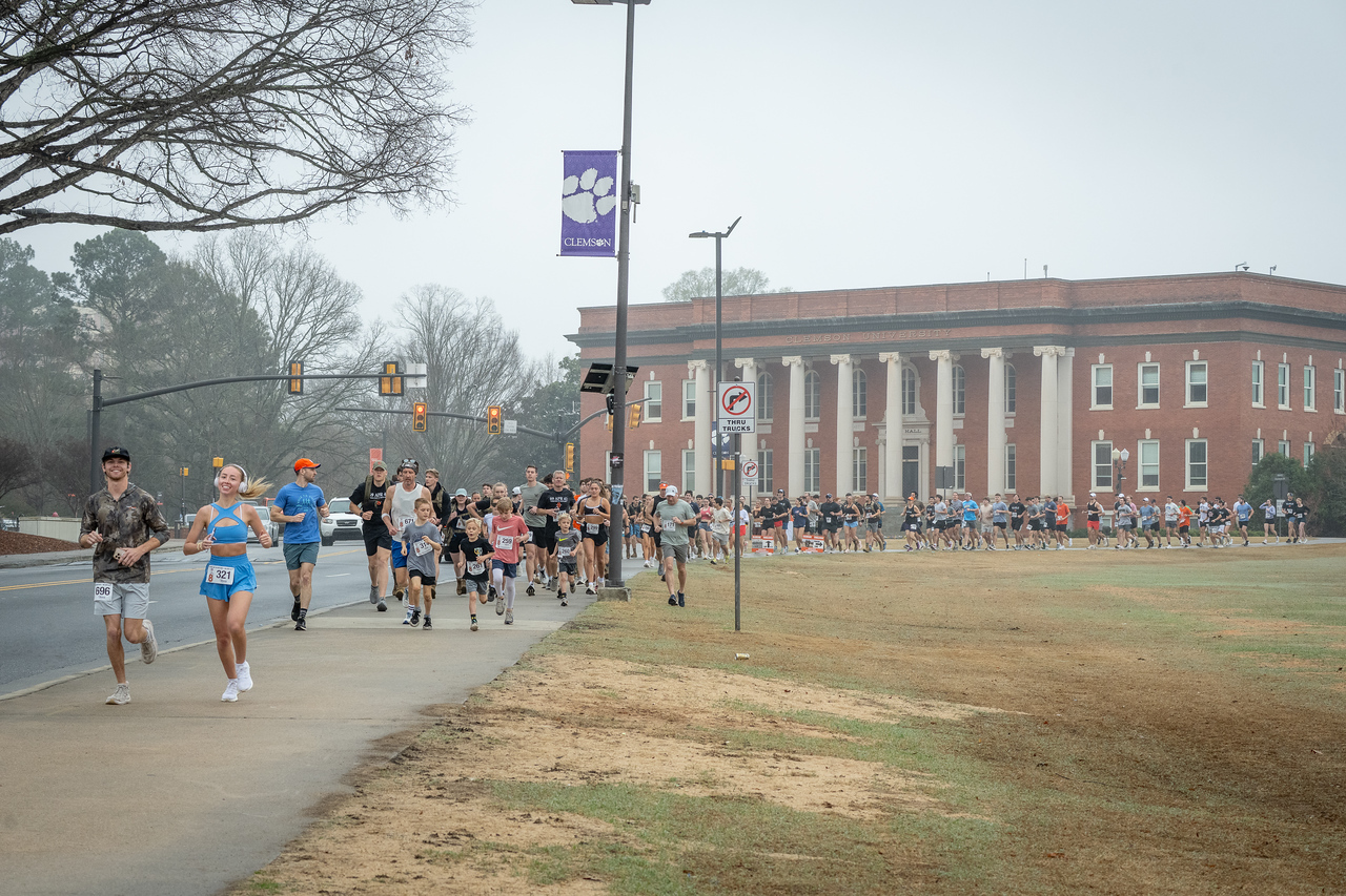 Hundreds of people participate in the 2026 Clemson 8 Challenge, an eight-mile run/walk/ruck march, on a misty Saturday morning, March 7, 2026. The Challenge was created to honor the 25 known Clemson alumni who suffered as POWs in all wars. It was originally created for 1938 Clemson alumnus, professor emeritus and WWII hero Ben Skardon, a survivor of the Bataan Death March, but has expanded to include Clemson POWs from all wars. Money raised from the event goes toward sending teams of Clemson ROTC students to participate in the Bataan Memorial Death March at White Sands Missile Range, NM. Sophomore finance major GB Stalnaker served as master of ceremonies. (Photo by Ken Scar)