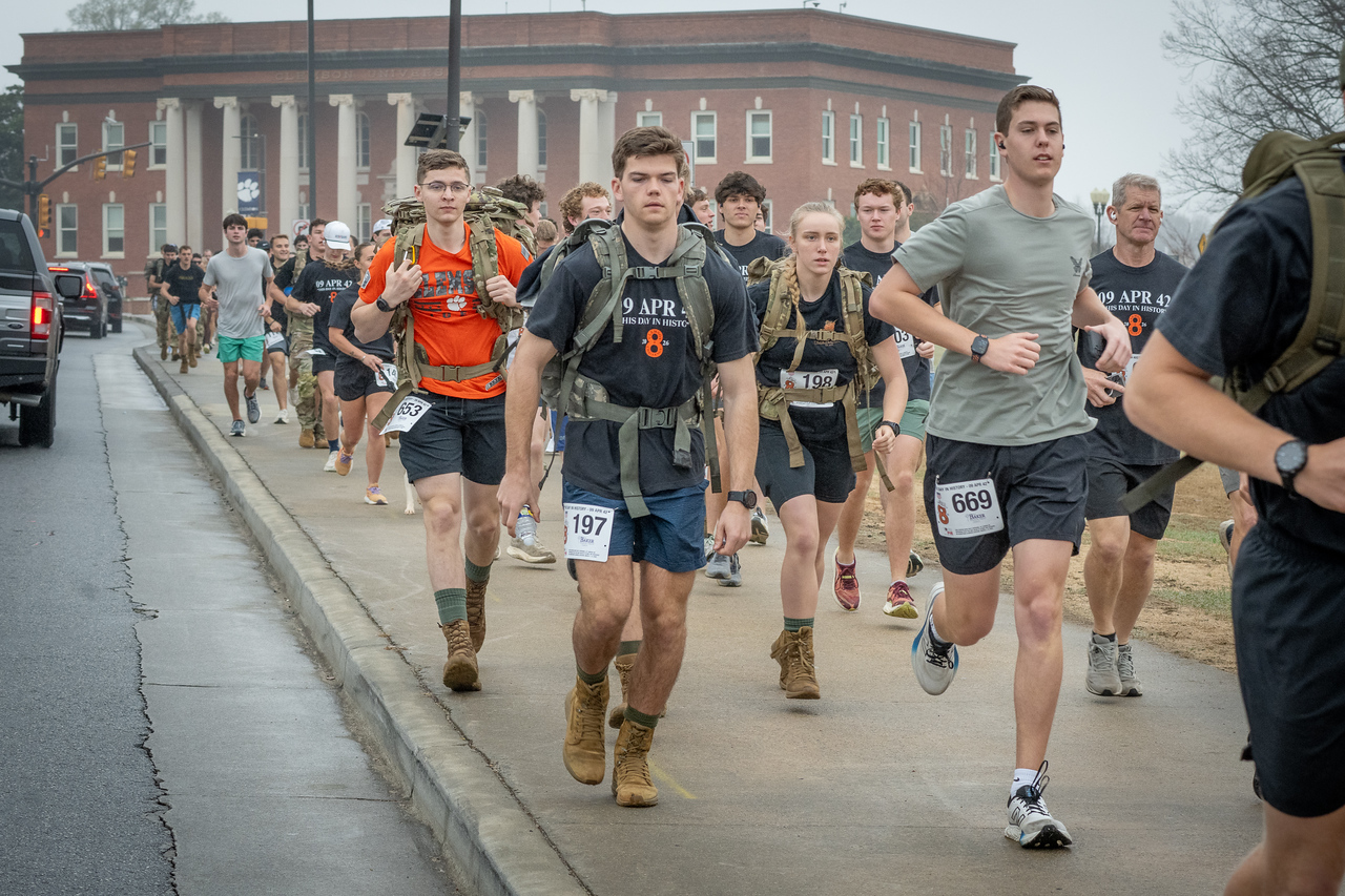 Hundreds of people participate in the 2026 Clemson 8 Challenge, an eight-mile run/walk/ruck march, on a misty Saturday morning, March 7, 2026. The Challenge was created to honor the 25 known Clemson alumni who suffered as POWs in all wars. It was originally created for 1938 Clemson alumnus, professor emeritus and WWII hero Ben Skardon, a survivor of the Bataan Death March, but has expanded to include Clemson POWs from all wars. Money raised from the event goes toward sending teams of Clemson ROTC students to participate in the Bataan Memorial Death March at White Sands Missile Range, NM. Sophomore finance major GB Stalnaker served as master of ceremonies. (Photo by Ken Scar)
