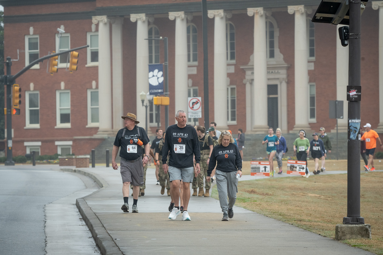 Hundreds of people participate in the 2026 Clemson 8 Challenge, an eight-mile run/walk/ruck march, on a misty Saturday morning, March 7, 2026. The Challenge was created to honor the 25 known Clemson alumni who suffered as POWs in all wars. It was originally created for 1938 Clemson alumnus, professor emeritus and WWII hero Ben Skardon, a survivor of the Bataan Death March, but has expanded to include Clemson POWs from all wars. Money raised from the event goes toward sending teams of Clemson ROTC students to participate in the Bataan Memorial Death March at White Sands Missile Range, NM. Sophomore finance major GB Stalnaker served as master of ceremonies. (Photo by Ken Scar)
