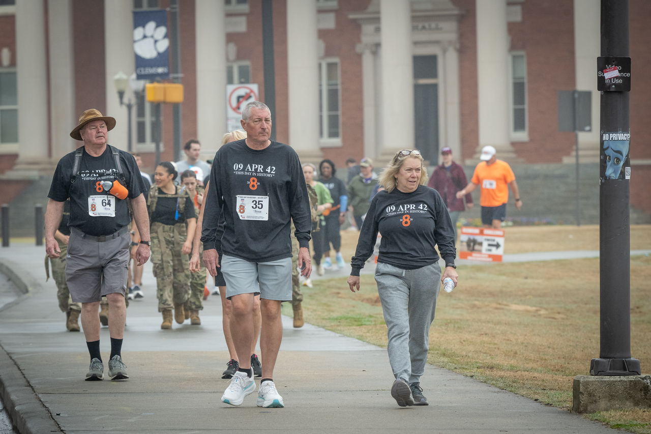 Hundreds of people participate in the 2026 Clemson 8 Challenge, an eight-mile run/walk/ruck march, on a misty Saturday morning, March 7, 2026. The Challenge was created to honor the 25 known Clemson alumni who suffered as POWs in all wars. It was originally created for 1938 Clemson alumnus, professor emeritus and WWII hero Ben Skardon, a survivor of the Bataan Death March, but has expanded to include Clemson POWs from all wars. Money raised from the event goes toward sending teams of Clemson ROTC students to participate in the Bataan Memorial Death March at White Sands Missile Range, NM. Sophomore finance major GB Stalnaker served as master of ceremonies. (Photo by Ken Scar)